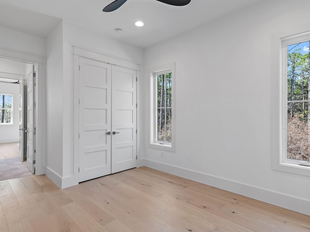 unfurnished bedroom featuring multiple windows, light hardwood / wood-style flooring, a closet, and ceiling fan