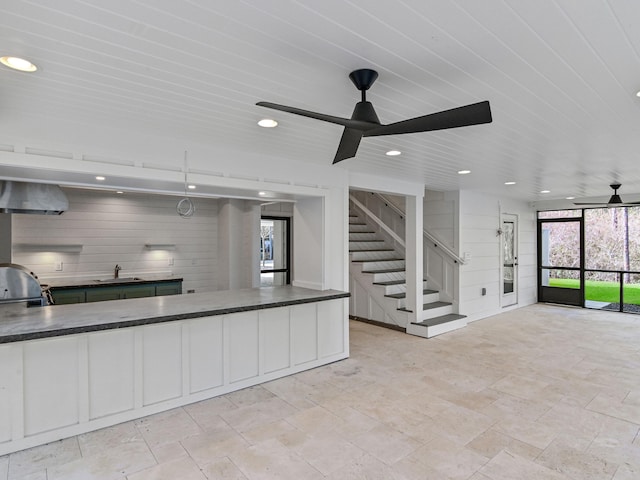 kitchen with white cabinets, ceiling fan, sink, and wall chimney range hood