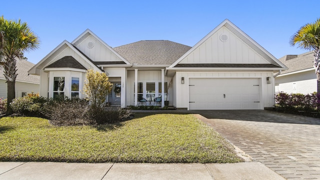 view of front facade with decorative driveway, roof with shingles, an attached garage, board and batten siding, and a front lawn