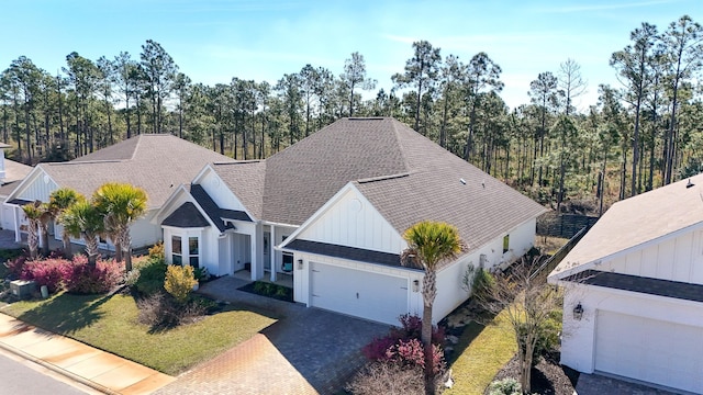 view of front of property with an attached garage, driveway, roof with shingles, a front lawn, and board and batten siding