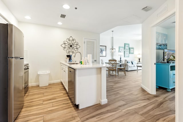 kitchen featuring stainless steel appliances, kitchen peninsula, light hardwood / wood-style floors, and hanging light fixtures