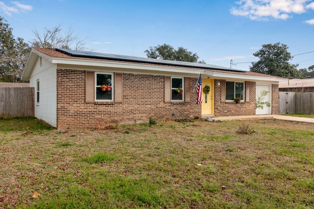 ranch-style home featuring an attached garage, fence, roof mounted solar panels, a front lawn, and brick siding