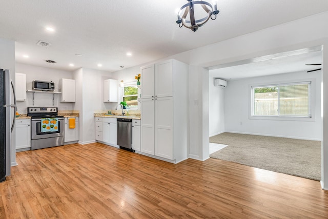 kitchen with a healthy amount of sunlight, appliances with stainless steel finishes, open floor plan, light wood-type flooring, and a wall mounted AC