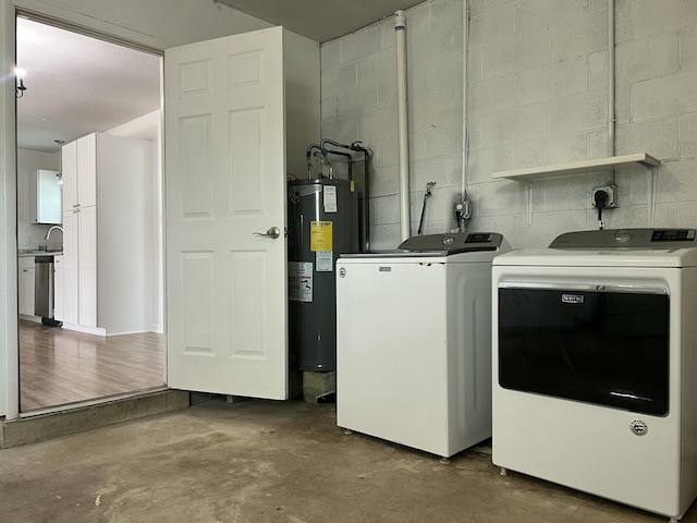 washroom with concrete block wall, water heater, a sink, separate washer and dryer, and laundry area