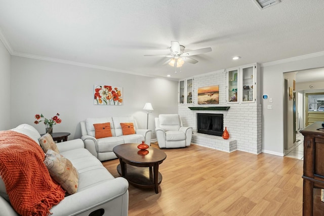 living room with light wood-type flooring, ornamental molding, ceiling fan, a brick fireplace, and a textured ceiling