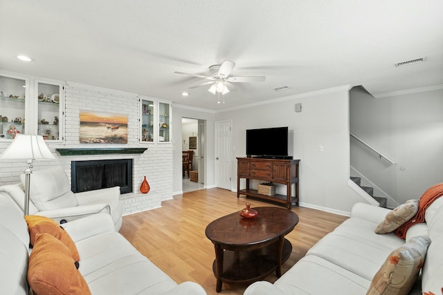 living room with built in features, ceiling fan, crown molding, a brick fireplace, and light hardwood / wood-style flooring