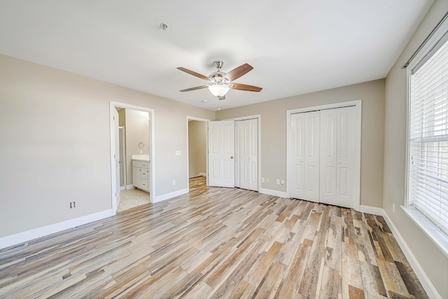 unfurnished bedroom with ceiling fan, connected bathroom, two closets, and light hardwood / wood-style floors