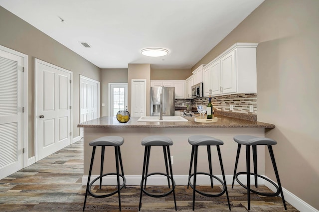 kitchen featuring white cabinetry, backsplash, a kitchen bar, kitchen peninsula, and stainless steel appliances