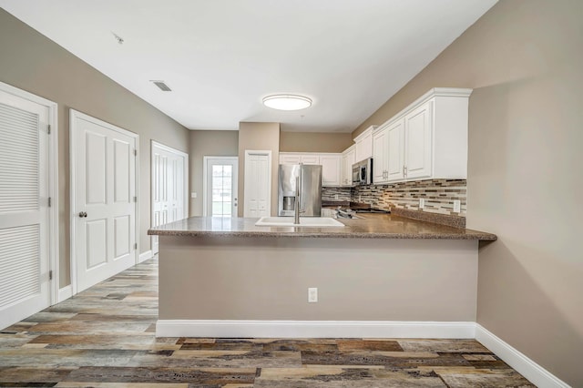 kitchen featuring wood-type flooring, appliances with stainless steel finishes, kitchen peninsula, decorative backsplash, and white cabinets