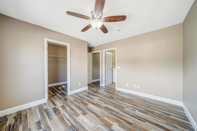 unfurnished bedroom with ceiling fan, a walk in closet, hardwood / wood-style floors, and a closet