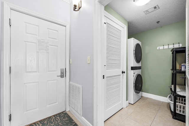 laundry area featuring stacked washer and dryer, light tile patterned floors, and a textured ceiling