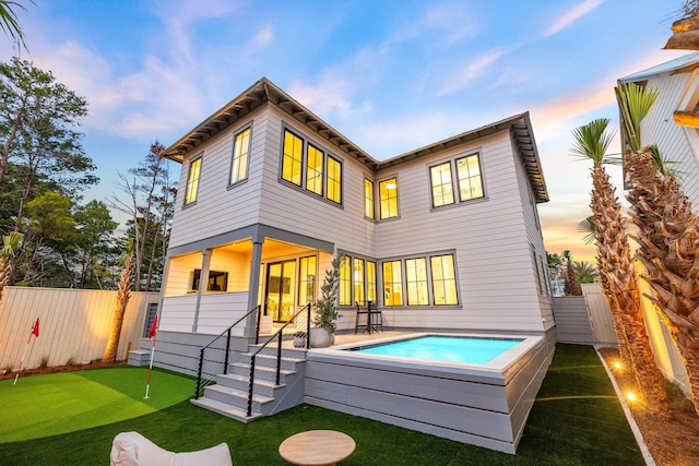 back of property at dusk with a pool and a fenced backyard