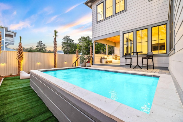 pool at dusk featuring an outdoor living space and a patio