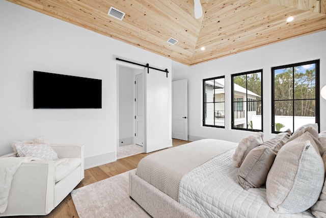 bedroom featuring wood ceiling, a barn door, a high ceiling, and light wood-type flooring