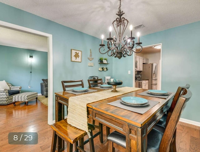 dining room featuring a notable chandelier, light hardwood / wood-style flooring, and a textured ceiling