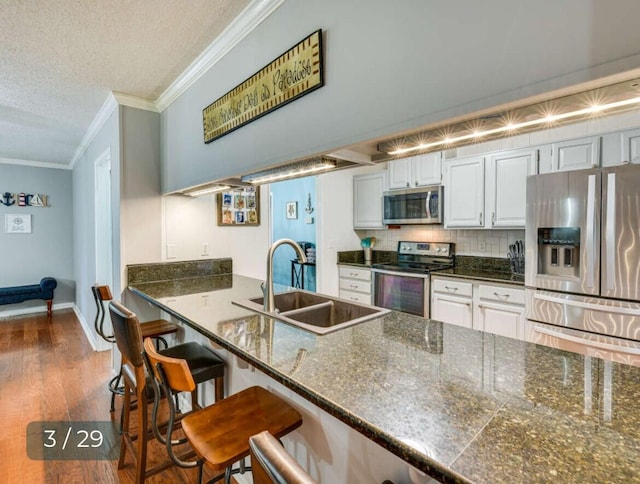 kitchen with sink, a breakfast bar area, white cabinets, ornamental molding, and stainless steel appliances