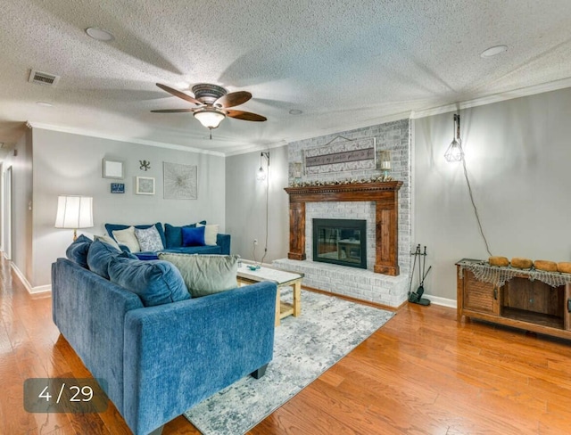 living room with hardwood / wood-style floors, ceiling fan, crown molding, a brick fireplace, and a textured ceiling