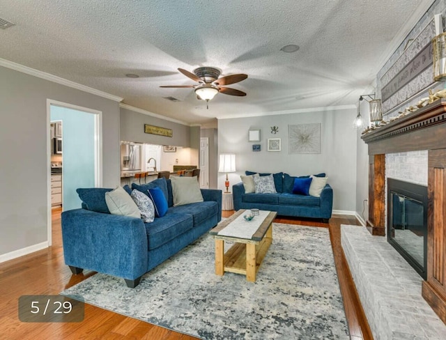 living room with hardwood / wood-style flooring, crown molding, a brick fireplace, and a textured ceiling