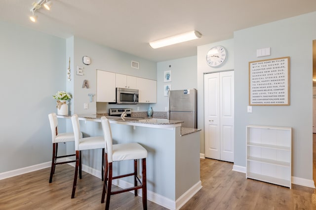 kitchen with appliances with stainless steel finishes, white cabinetry, a kitchen bar, kitchen peninsula, and light wood-type flooring