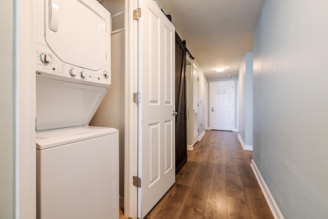 clothes washing area with hardwood / wood-style flooring, stacked washing maching and dryer, and a barn door