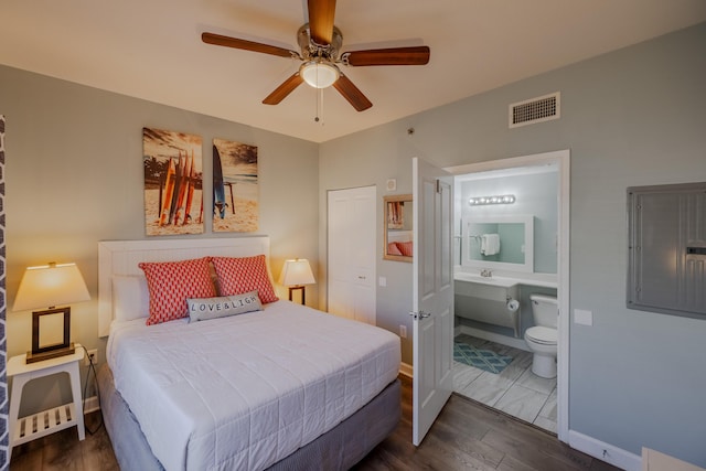 bedroom featuring dark wood-type flooring, ensuite bath, electric panel, and ceiling fan