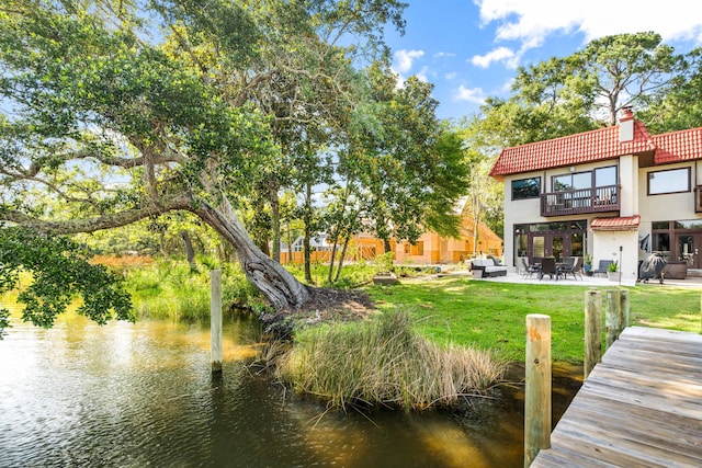 dock area with a patio, a balcony, a lawn, a water view, and an outdoor living space