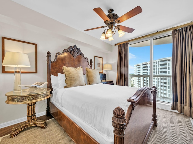 bedroom featuring ceiling fan, a city view, wood finished floors, baseboards, and access to exterior