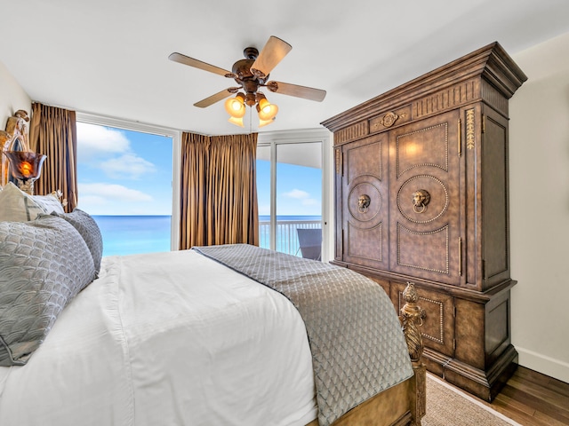 bedroom featuring access to exterior, a water view, a ceiling fan, wood finished floors, and baseboards