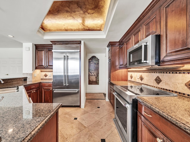 kitchen featuring appliances with stainless steel finishes, a tray ceiling, dark stone counters, and a sink