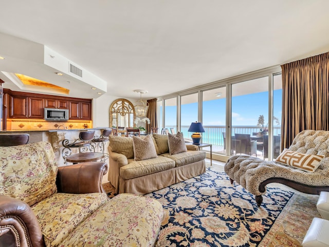 living room featuring a tray ceiling, a wall of windows, a water view, and visible vents