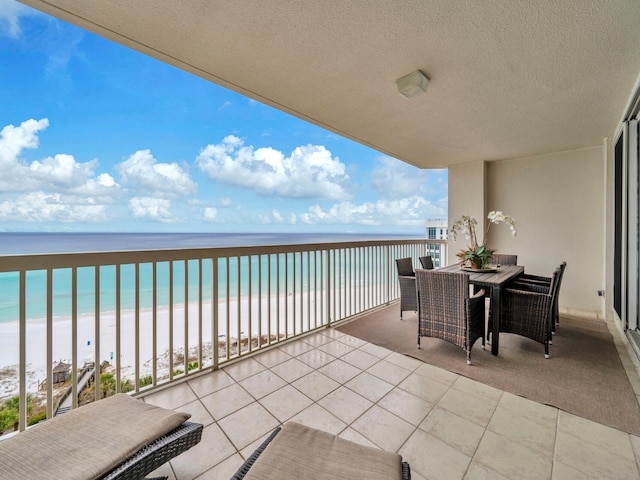 balcony with outdoor dining area, a beach view, and a water view