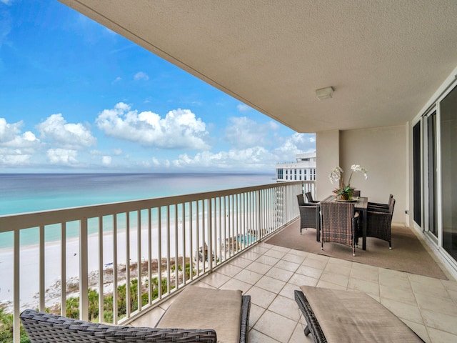 balcony featuring outdoor dining area, a water view, and a beach view