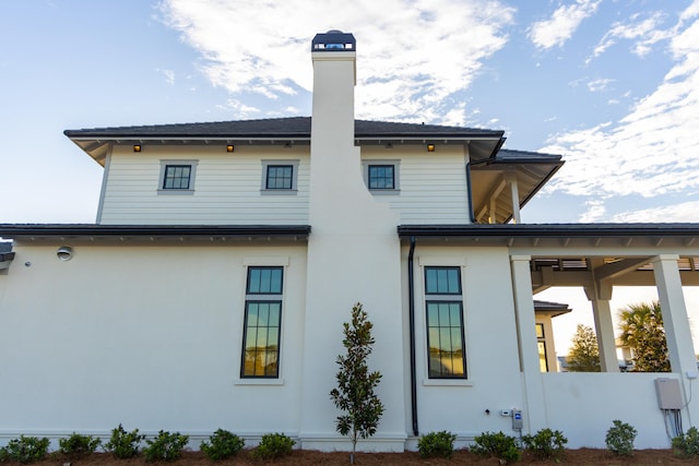 rear view of property with a chimney and stucco siding