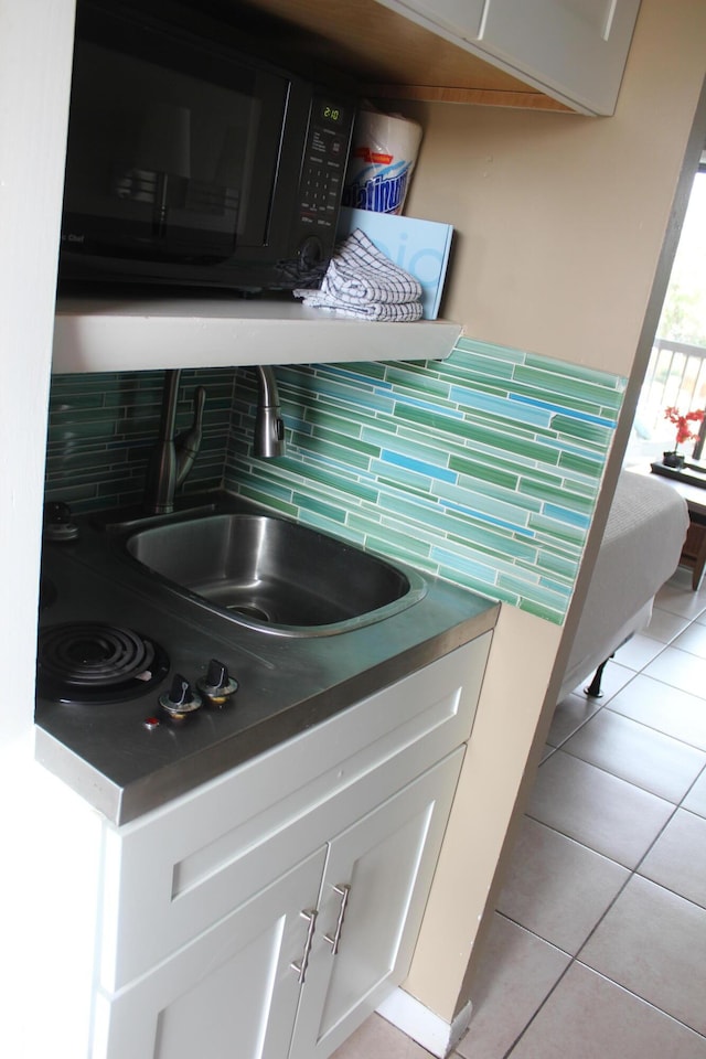 room details featuring tasteful backsplash, white cabinets, black microwave, and a sink