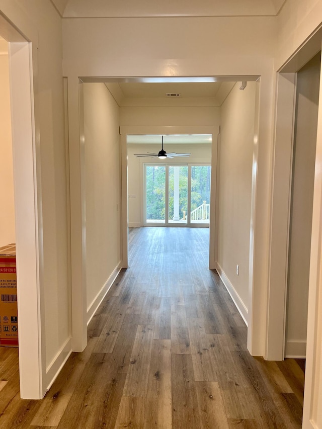 hallway with ornamental molding, wood finished floors, visible vents, and baseboards