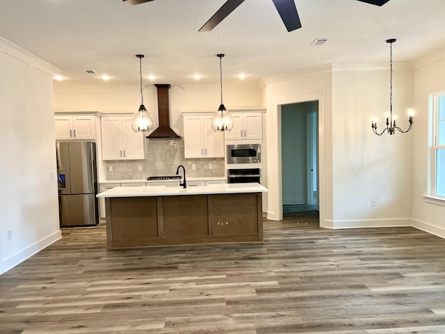 kitchen with visible vents, an island with sink, wall chimney exhaust hood, stainless steel appliances, and light countertops