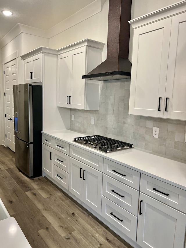 kitchen featuring white cabinets, wall chimney exhaust hood, appliances with stainless steel finishes, light countertops, and light wood-type flooring