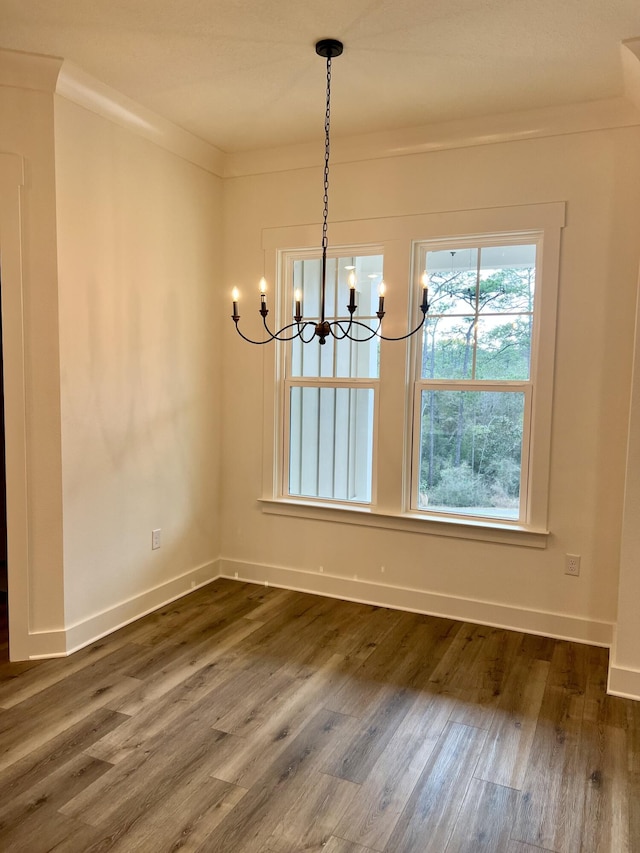 unfurnished dining area with ornamental molding, dark wood-style flooring, baseboards, and an inviting chandelier