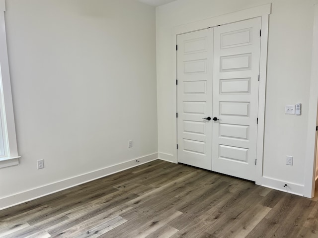 unfurnished bedroom with dark wood-style flooring, a closet, and baseboards