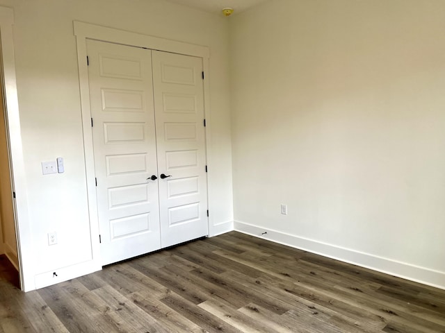 unfurnished bedroom with a closet, dark wood finished floors, and baseboards