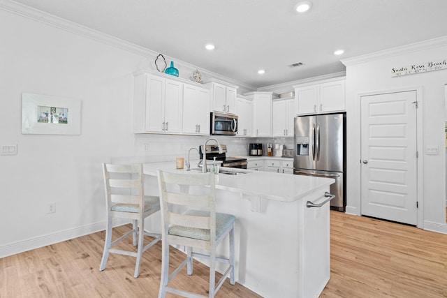 kitchen featuring appliances with stainless steel finishes, a kitchen bar, kitchen peninsula, and white cabinets