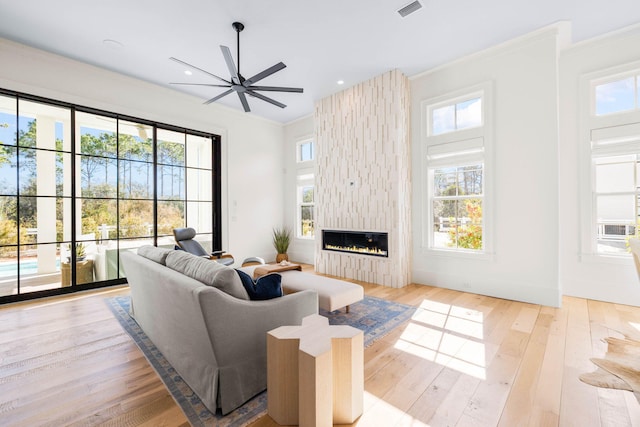 living room featuring crown molding, a large fireplace, ceiling fan, and light hardwood / wood-style floors