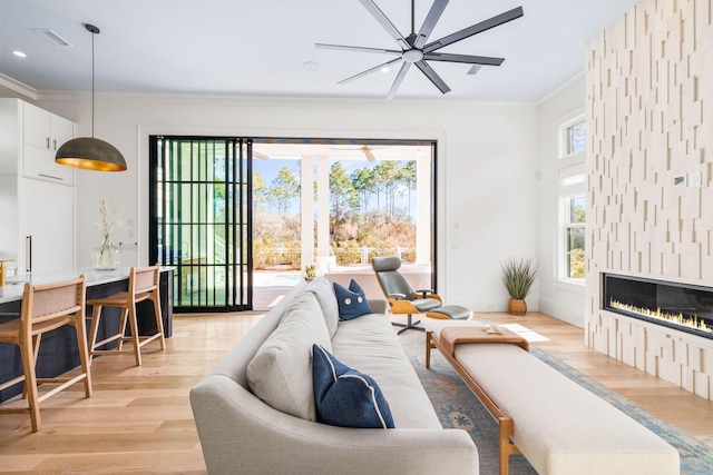 living room with crown molding, a large fireplace, light hardwood / wood-style flooring, and a wealth of natural light