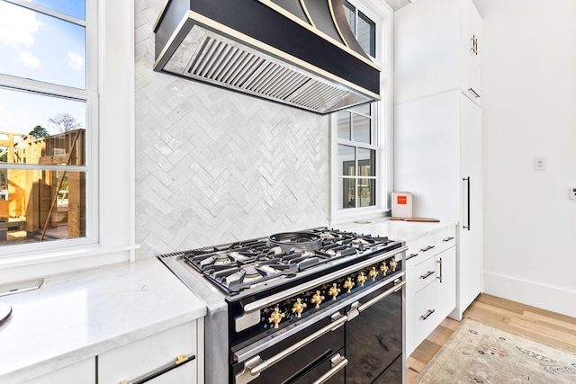 kitchen featuring white cabinets, range with two ovens, custom exhaust hood, light stone countertops, and light wood-type flooring