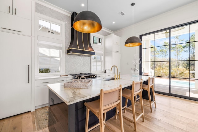 kitchen featuring white cabinetry, sink, decorative light fixtures, and an island with sink