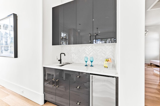 bar featuring tasteful backsplash, sink, wine cooler, light stone counters, and light wood-type flooring