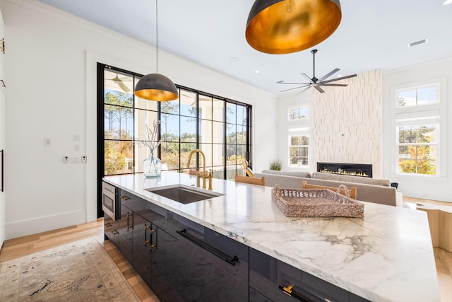 kitchen featuring sink, hanging light fixtures, a wealth of natural light, a fireplace, and light stone countertops