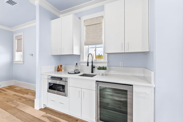 kitchen featuring crown molding, beverage cooler, sink, and white cabinets