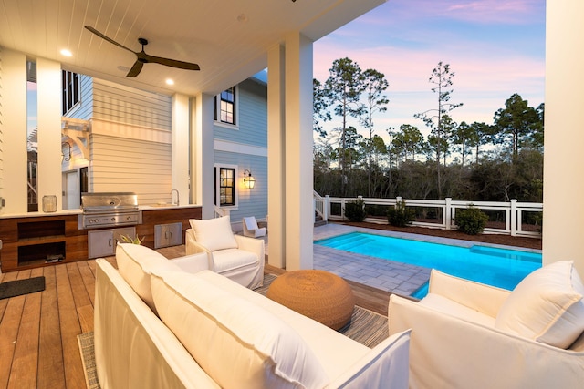 pool at dusk featuring exterior kitchen, ceiling fan, an outdoor living space, and grilling area