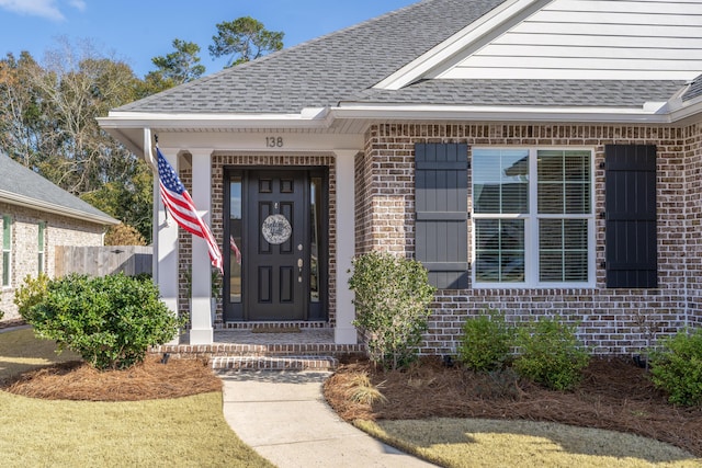 entrance to property featuring brick siding and roof with shingles